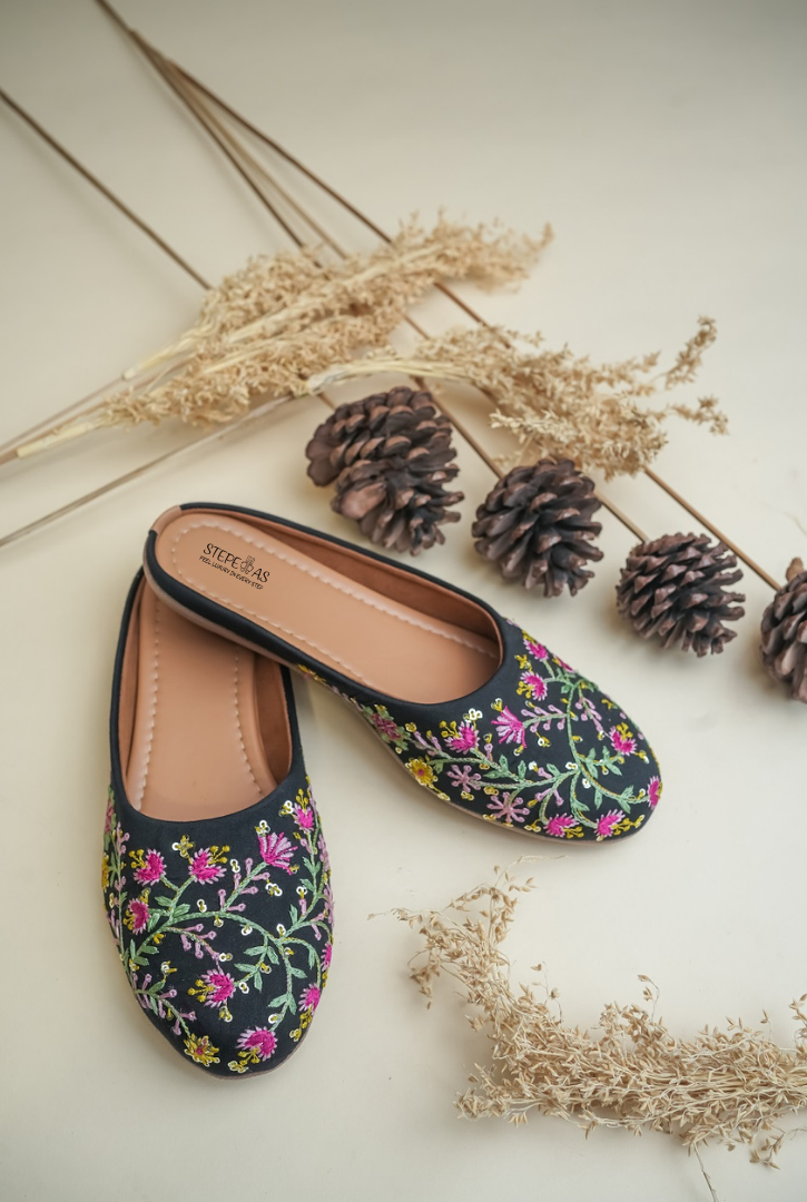 Stepellas black ethnic juttis featuring vibrant pink and yellow floral embroidery with green vine work.