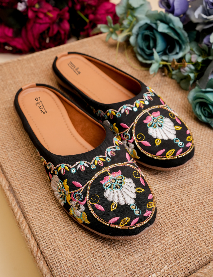 Stepellas black juttis featuring a large round mandala-style embroidery with pink and yellow threadwork.